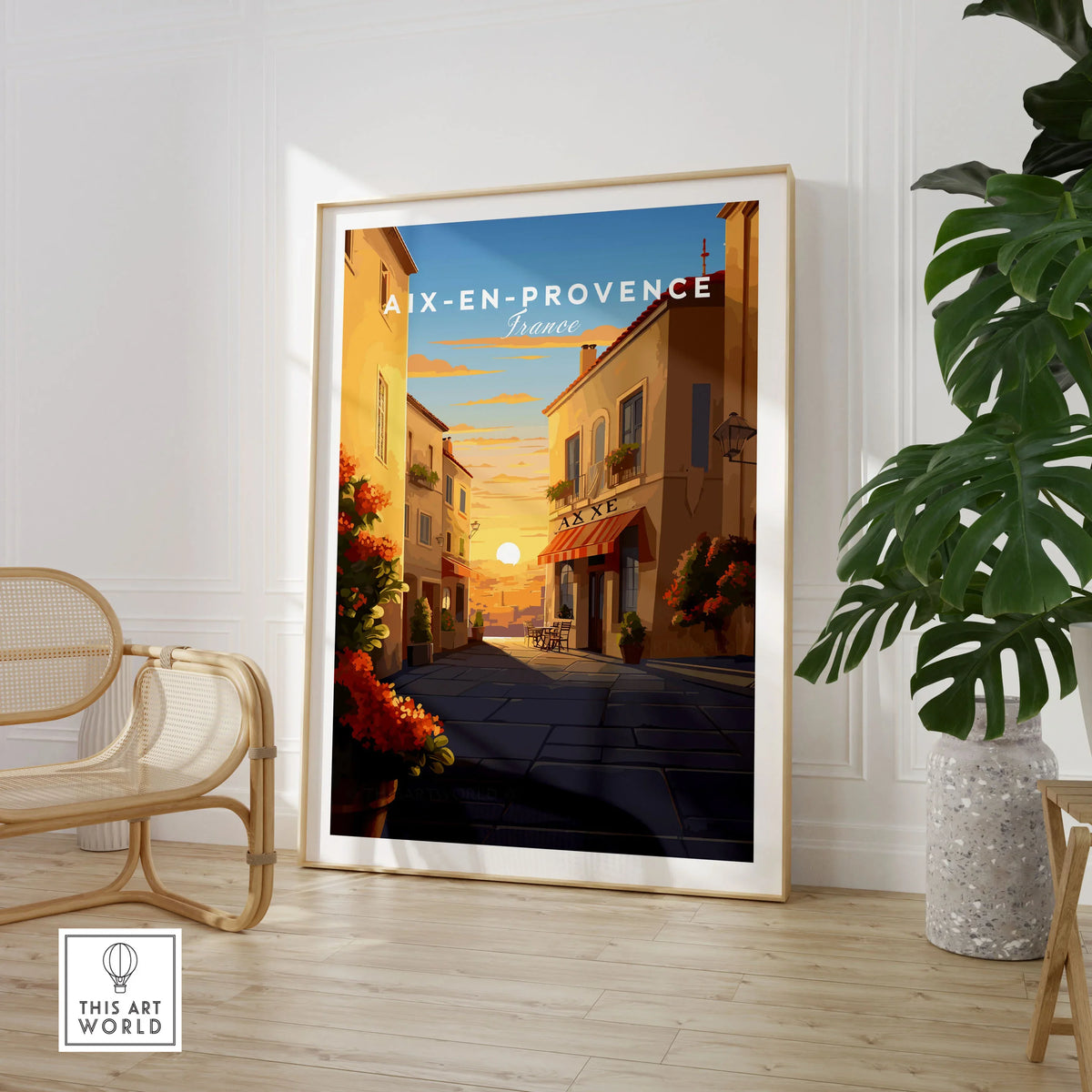 Aix-en-Provence Poster in a large natural wood frame leaning in a room with a rattan chair and monstera plant