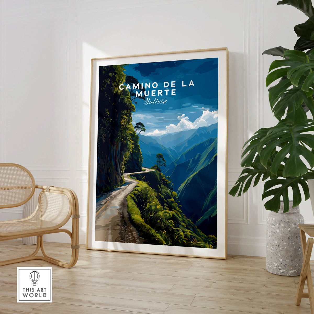 Camino de la Muerte Poster Bolivia Wall Art in a large natural wood frame leaning in a room with a rattan chair and monstera plant