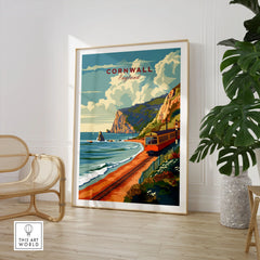 Cornwall Coast Travel Print in a large natural wood frame leaning in a room with a rattan chair and monstera plant