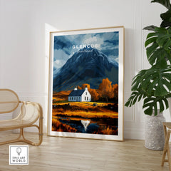 Glencoe Scotland Poster in a large natural wood frame leaning in a room with a rattan chair and monstera plant