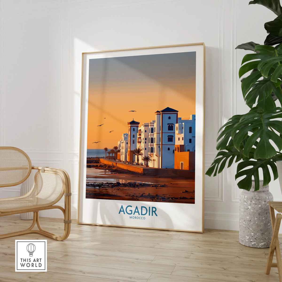 Agadir Morocco Wall Art in a large natural wood frame leaning in a room with a rattan chair and monstera plant