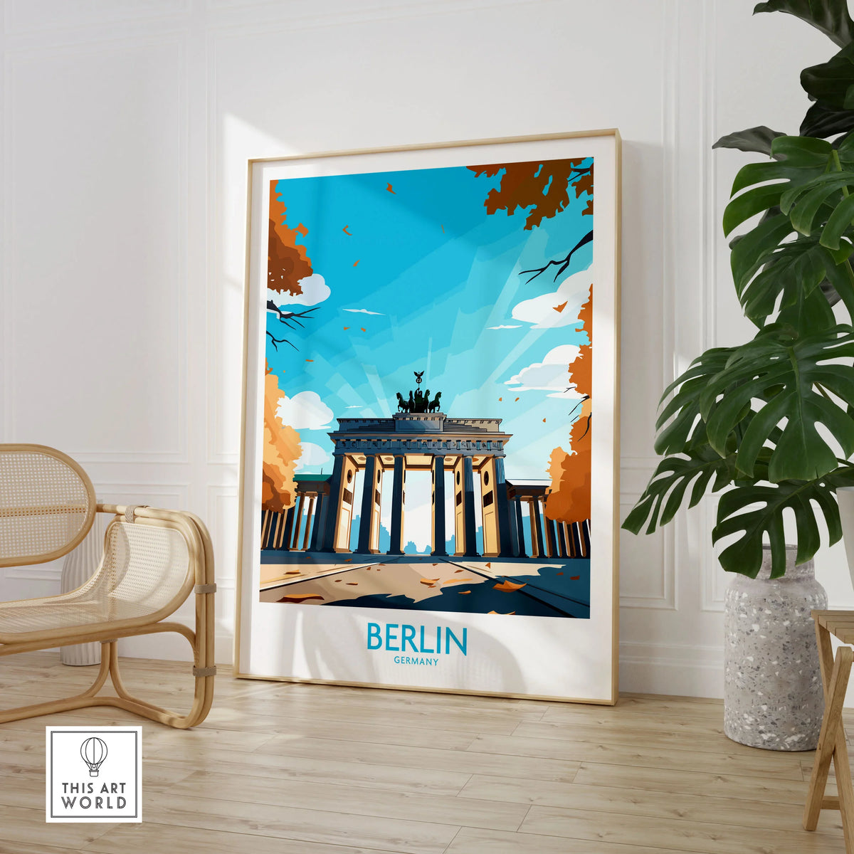 Berlin Wall Art Modern in a large natural wood frame leaning in a room with a rattan chair and monstera plant