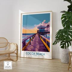 Cocoa Beach Florida Wooden Pier Poster - Golden Hour Sunset Decor in a large natural wood frame leaning in a room with a rattan chair and monstera plant