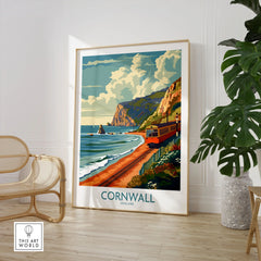 Cornwall Coast Wall Art Print in a large natural wood frame leaning in a room with a rattan chair and monstera plant