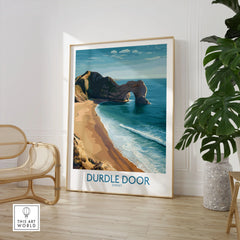 Durdle Door Art Print Dorset Wall Art in a large natural wood frame leaning in a room with a rattan chair and monstera plant