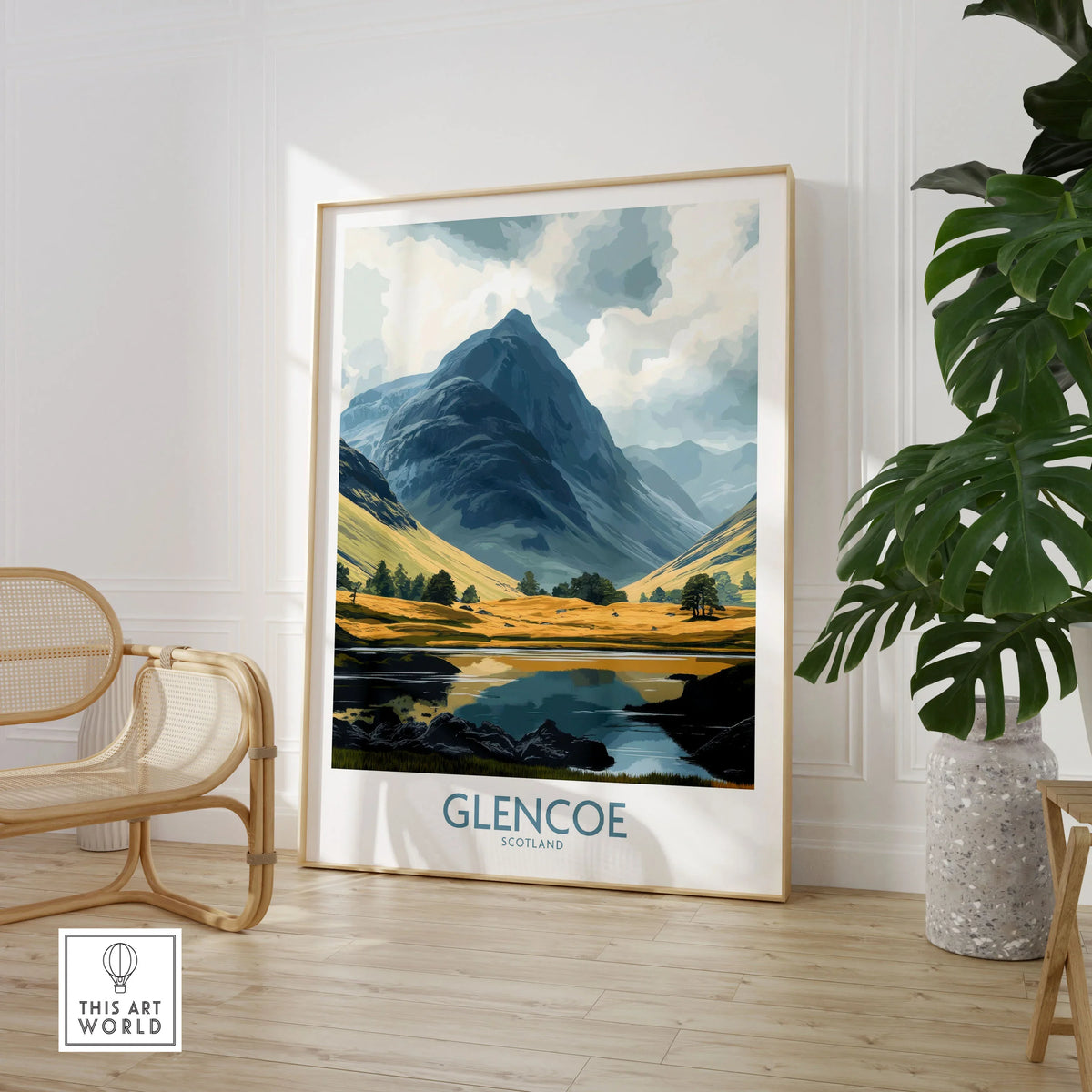 Glencoe Travel Poster in a large natural wood frame leaning in a room with a rattan chair and monstera plant