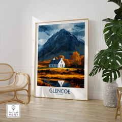 Glencoe Scotland Print in a large natural wood frame leaning in a room with a rattan chair and monstera plant