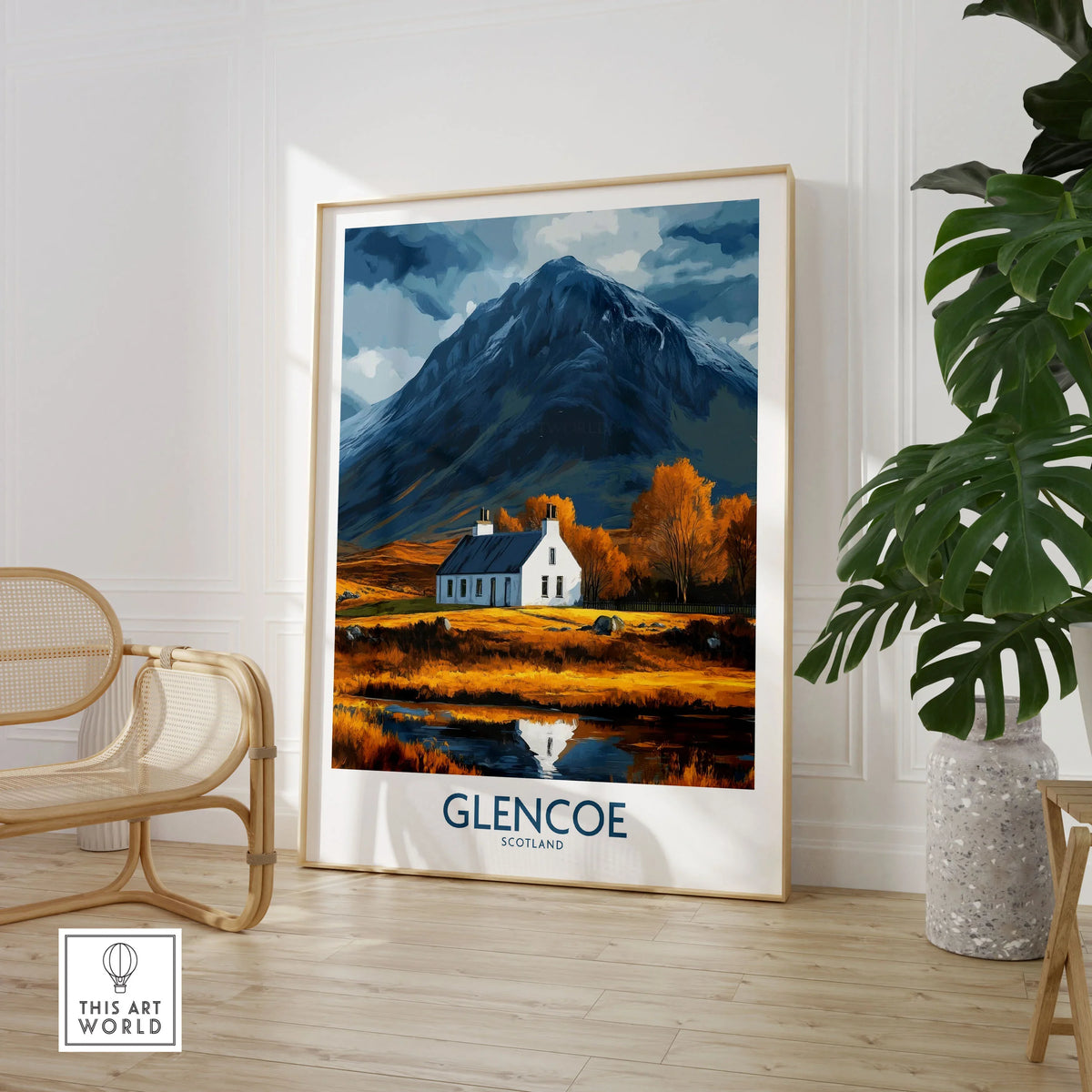 Glencoe Scotland Print in a large natural wood frame leaning in a room with a rattan chair and monstera plant
