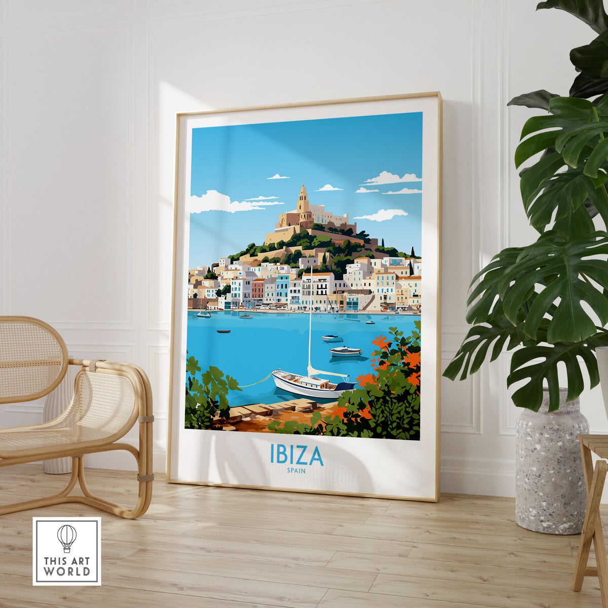 Ibiza Poster in a large natural wood frame leaning in a room with a rattan chair and monstera plant