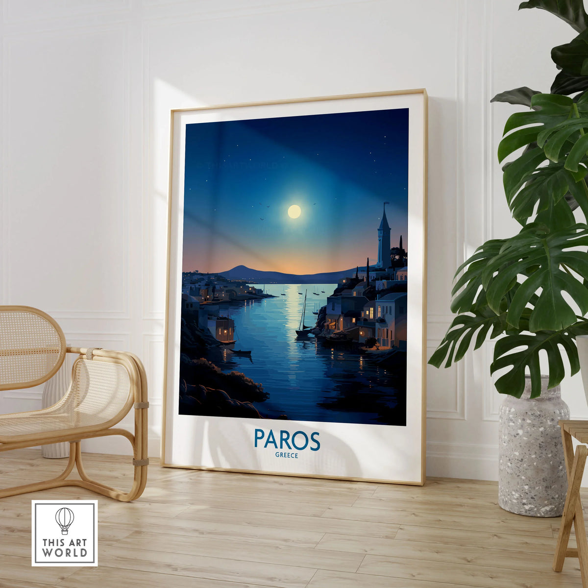 Paros Poster Greece in a large natural wood frame leaning in a room with a rattan chair and monstera plant