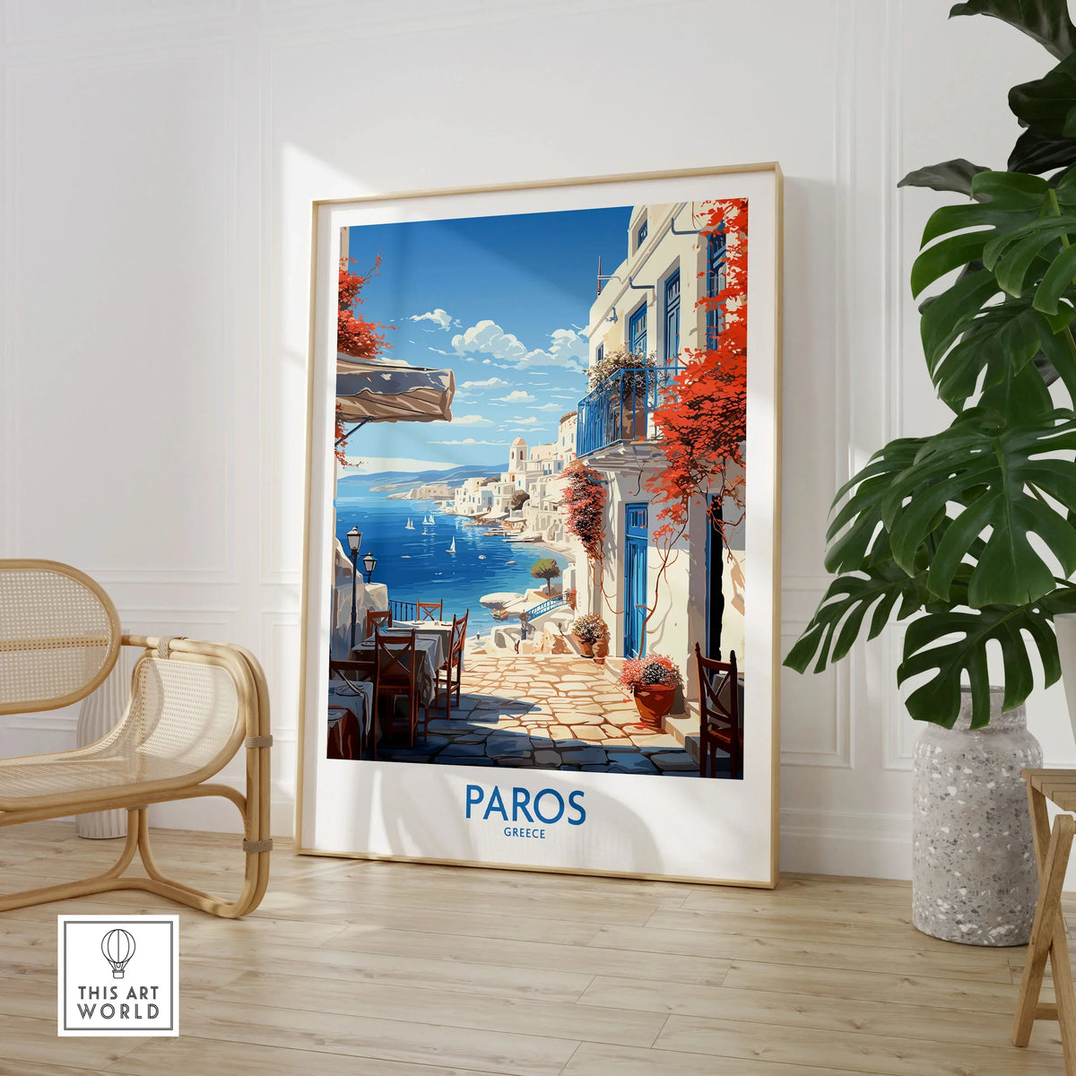 Paros Wall Art Greece in a large natural wood frame leaning in a room with a rattan chair and monstera plant