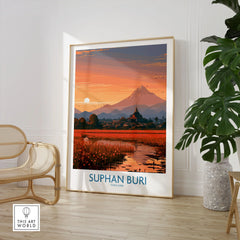Suphan Buri Thailand Temple Sunset Wall Art — a lotus-covered lake and temple spire at sunset beneath a mountain peak, shown as large framed print room setting chair plant