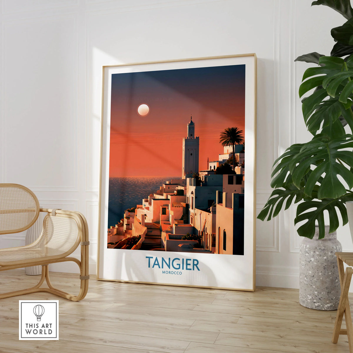 Tangier Morocco Coastal Sunset Wall Art — a whitewashed hillside town and minaret glowing above the sea at sunset, shown as large framed print room setting chair plant