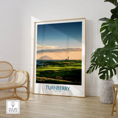 Turnberry Scotland Ayrshire Dusk Wall Art — Ailsa Craig and the white lighthouse across rolling coastal turf at dusk, shown as large framed print room setting chair plant