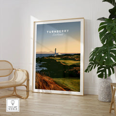 Turnberry Scotland Lighthouse Travel Poster — the Turnberry lighthouse above a rocky shore with the Arran hills beyond, shown as large framed print room setting chair plant