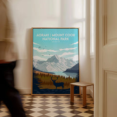 Framed Aoraki Mount Cook National Park travel poster with mountain and deer artwork on floor