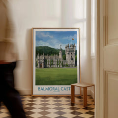 Framed Balmoral Castle travel poster on floor in bright hallway, man walking past