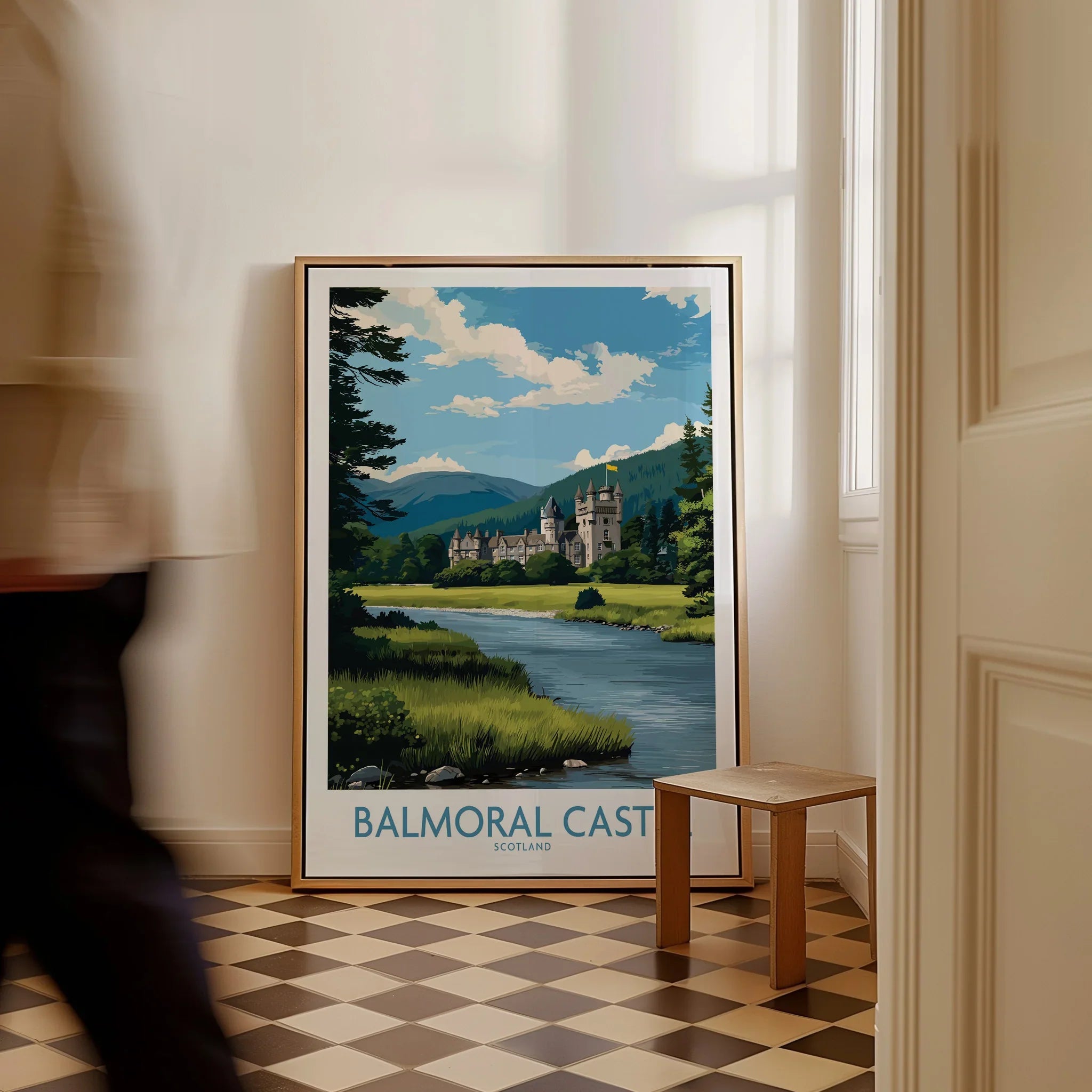 Framed Balmoral Castle travel poster on floor with man walking by in bright hallway