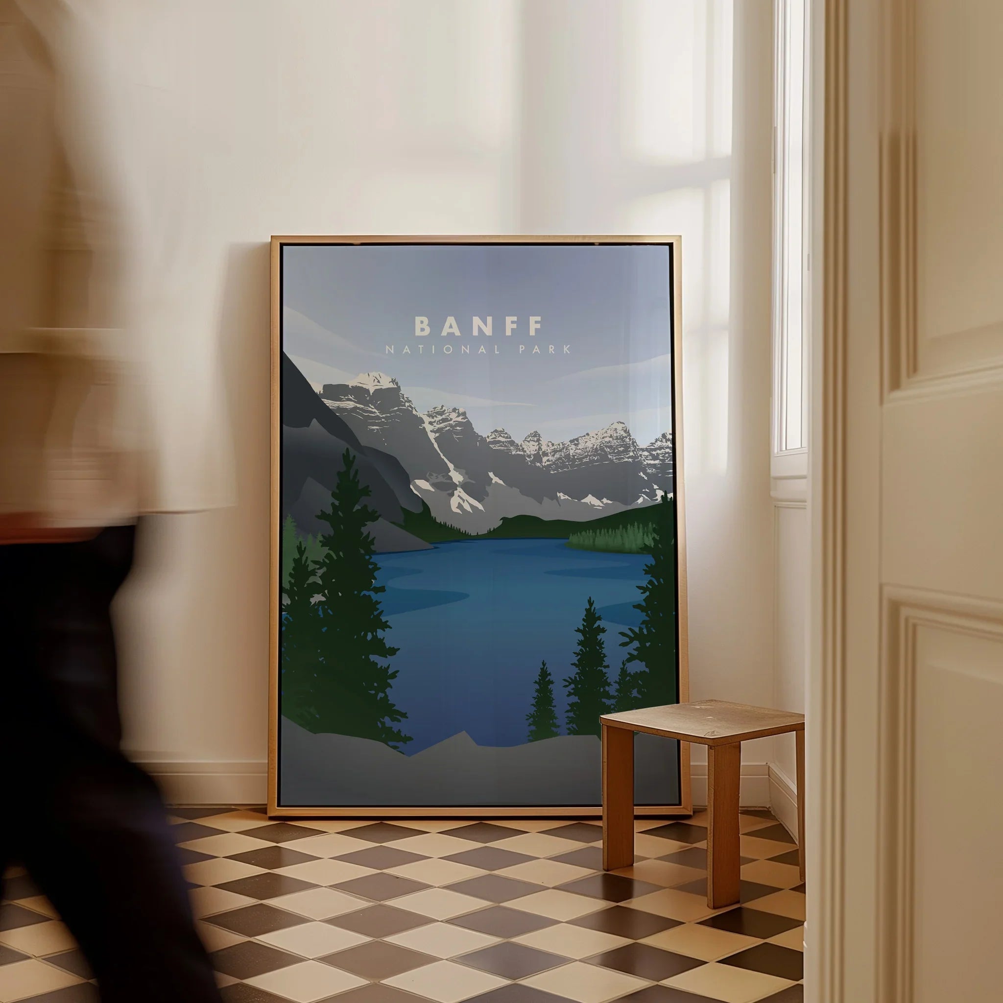 Framed Banff National Park travel poster with lake and mountains resting on floor in modern hallway