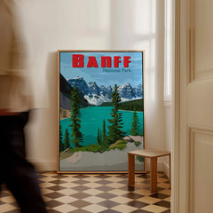 Framed Banff National Park travel poster with lake and mountains, leaning on wall indoors.