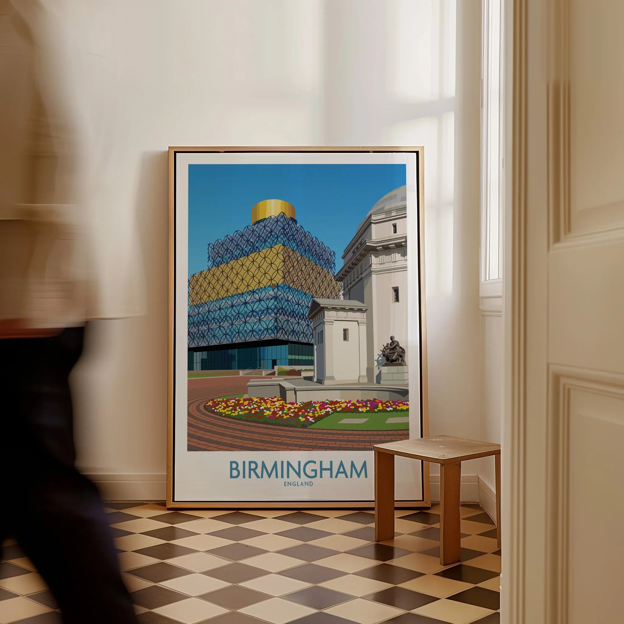 Framed Birmingham city travel poster on floor in bright entryway, man walking past