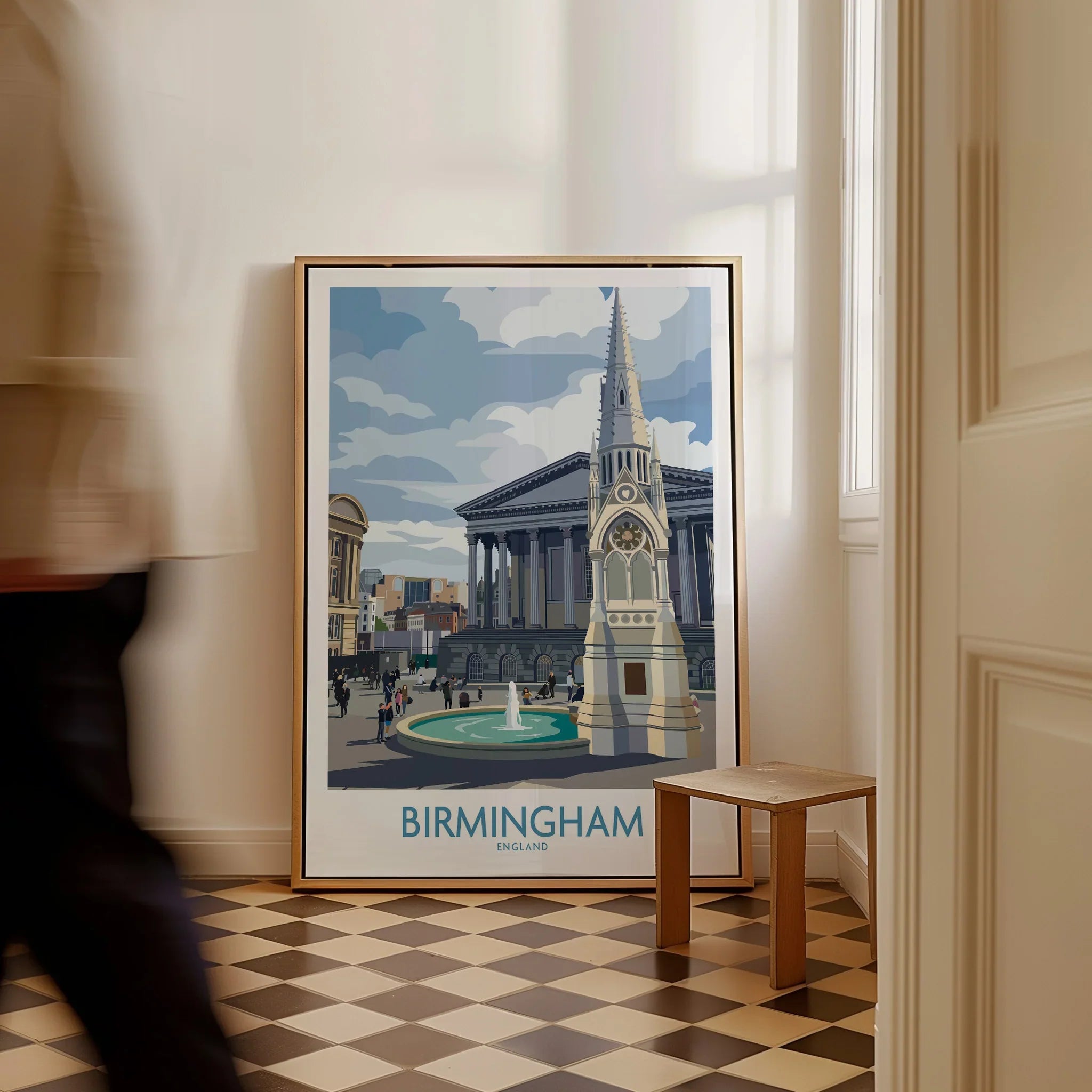 Framed Birmingham travel poster on floor, city skyline artwork, man walking past in hallway.