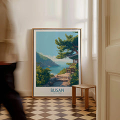 Framed Busan travel poster with coastal landscape art on floor in bright hallway