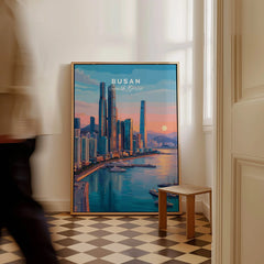 Framed Busan South Korea travel poster with city skyline art by a window on checkered floor.