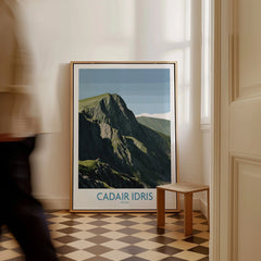 Framed Cadair Idris travel poster on checkered floor by a wall, man walking past.