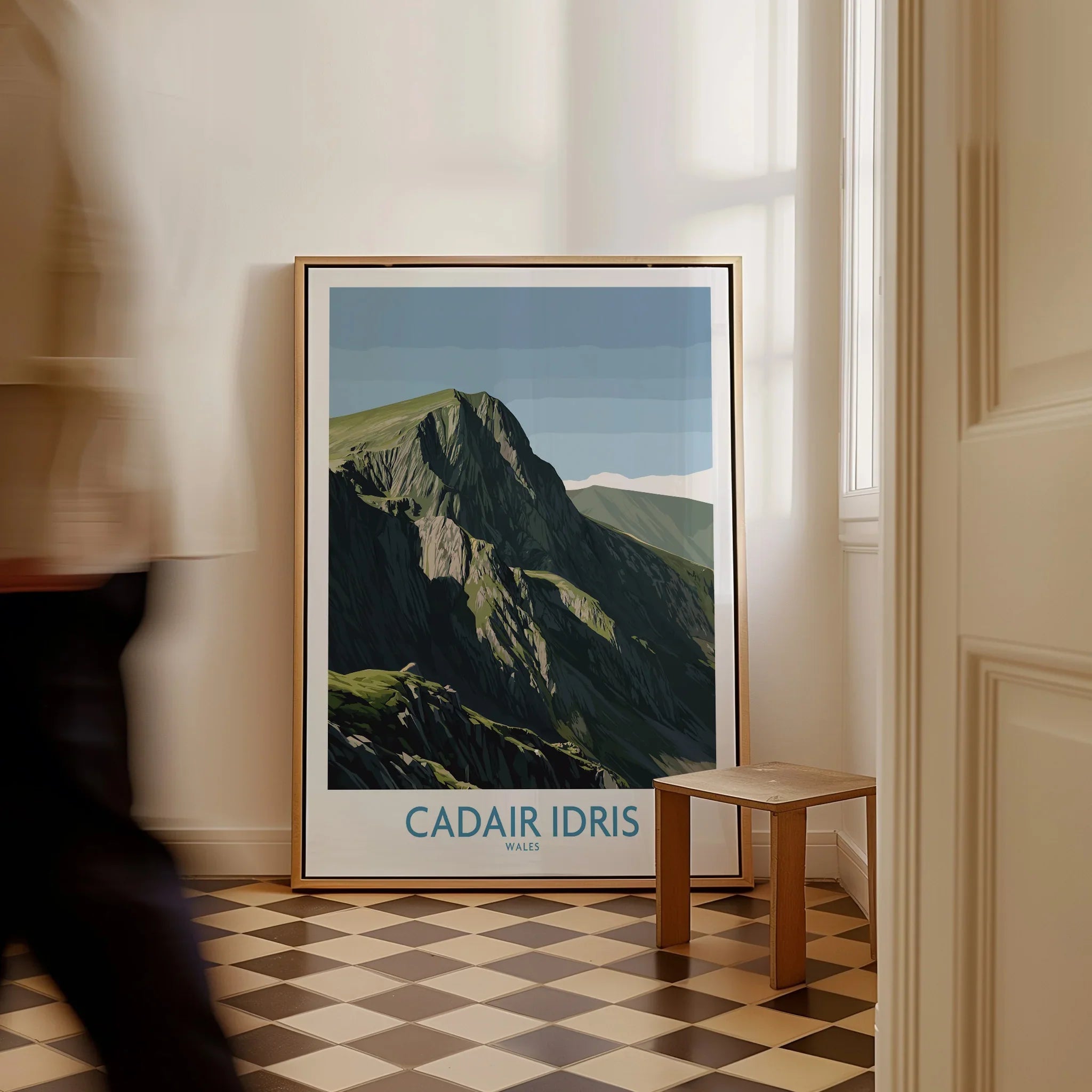 Framed Cadair Idris travel poster on checkered floor by a wall, man walking past.