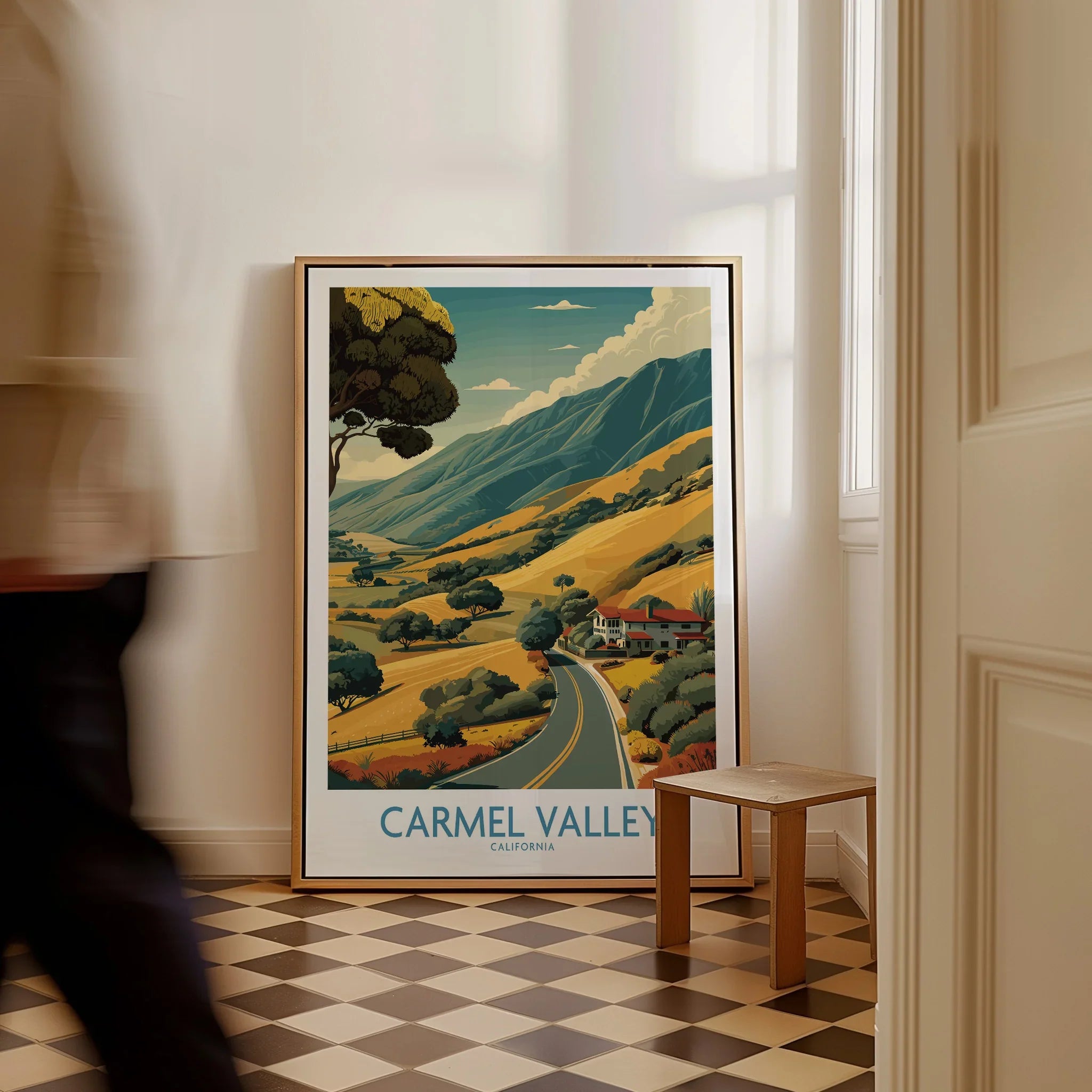 Framed Carmel Valley California travel poster with scenic landscape, leaning on floor in modern hallway.