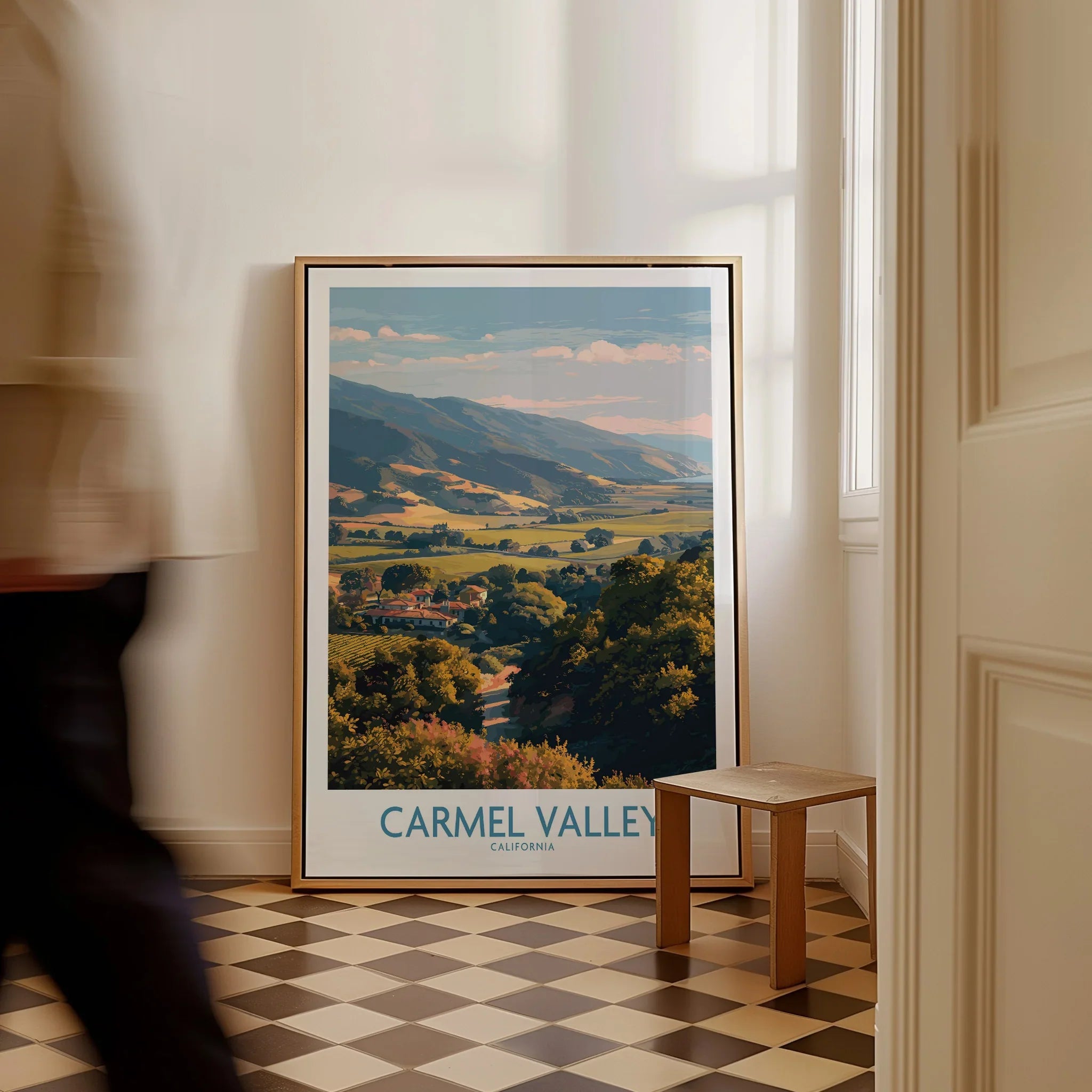 Framed Carmel Valley California wall art print on floor, checkered tile, person walking by.