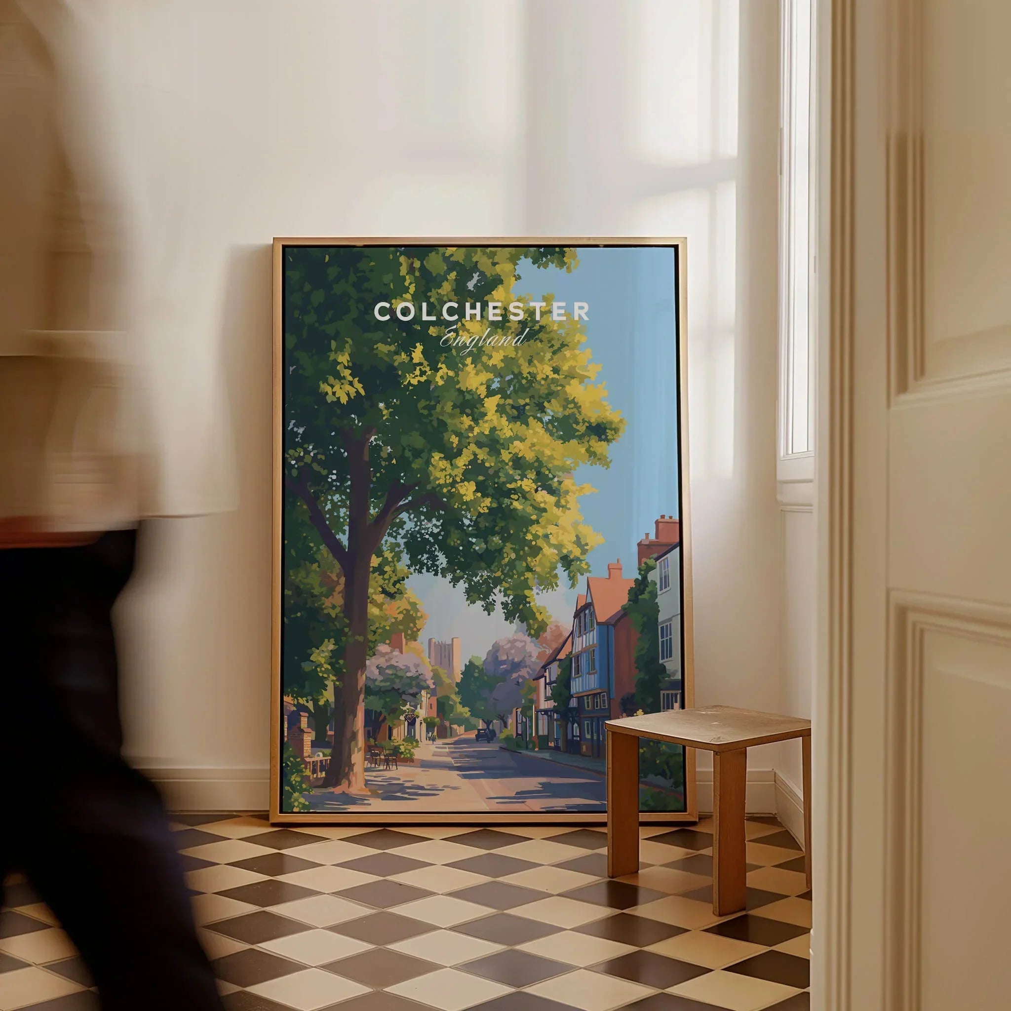 Framed Colchester travel poster with street scene leaning against wall, man walking past