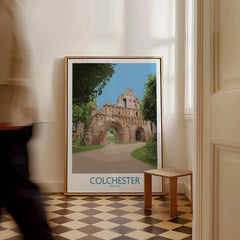 Framed Colchester travel poster with historic ruins, leaning on floor in modern home interior