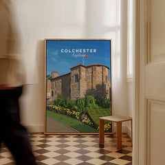 Framed Colchester England travel poster with castle art on floor in bright room