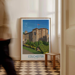 Framed Colchester England travel poster with castle illustration on floor in bright hallway.