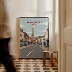 Framed Colchester travel poster on checkered floor, man walking past in modern home