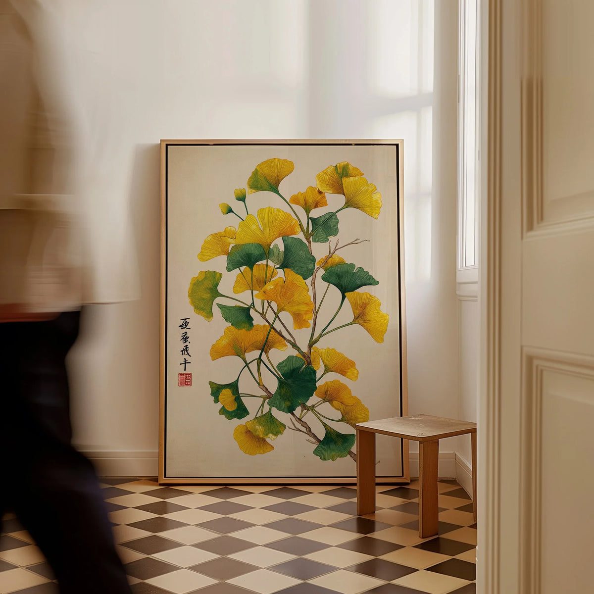 Framed botanical wall art with yellow and green ginkgo leaves on a floor in a bright room