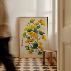 Framed botanical wall art with yellow and green ginkgo leaves on a floor in a bright room