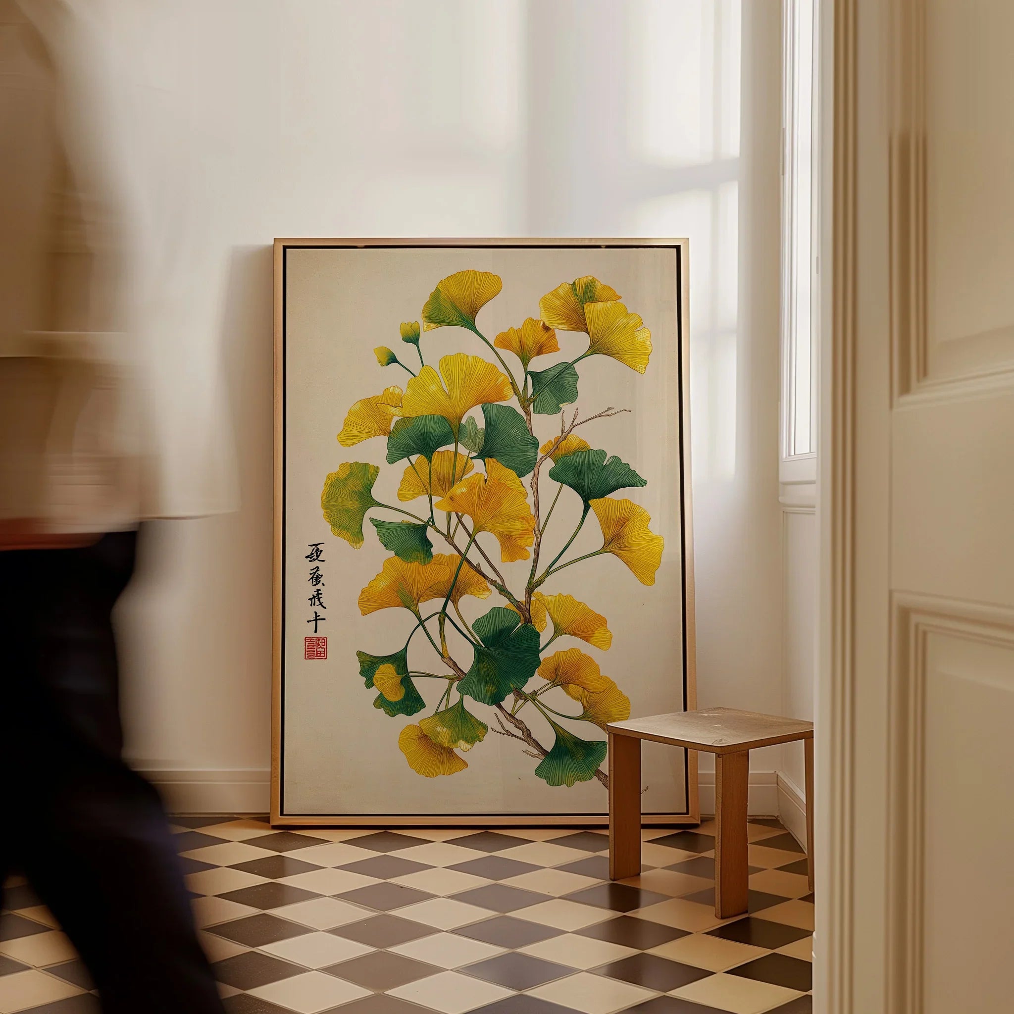 Framed botanical wall art with yellow and green ginkgo leaves on a floor in a bright room