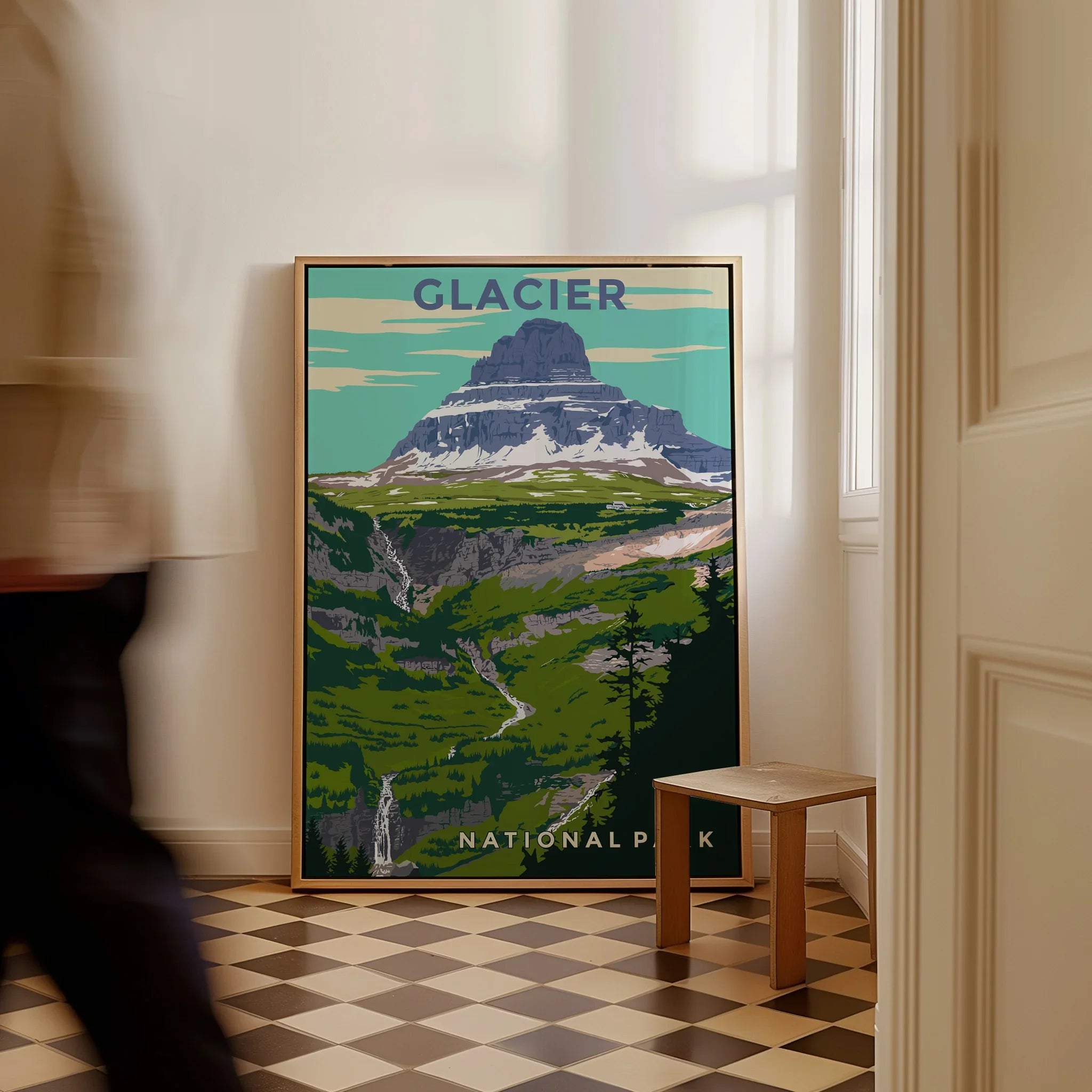 Framed Glacier National Park travel poster with mountain art on floor, man walking past