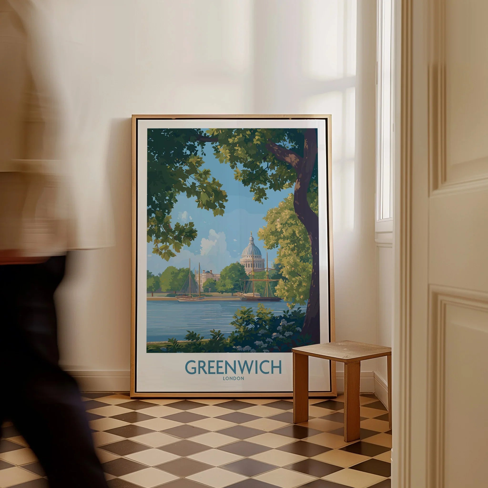 Framed Greenwich London travel poster art on floor with man walking past in bright hallway