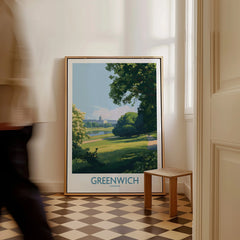 Framed Greenwich London travel poster with park scene, resting on floor in bright hallway.
