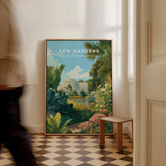 Framed Kew Gardens travel poster on checkered floor with greenery and a glasshouse illustration.