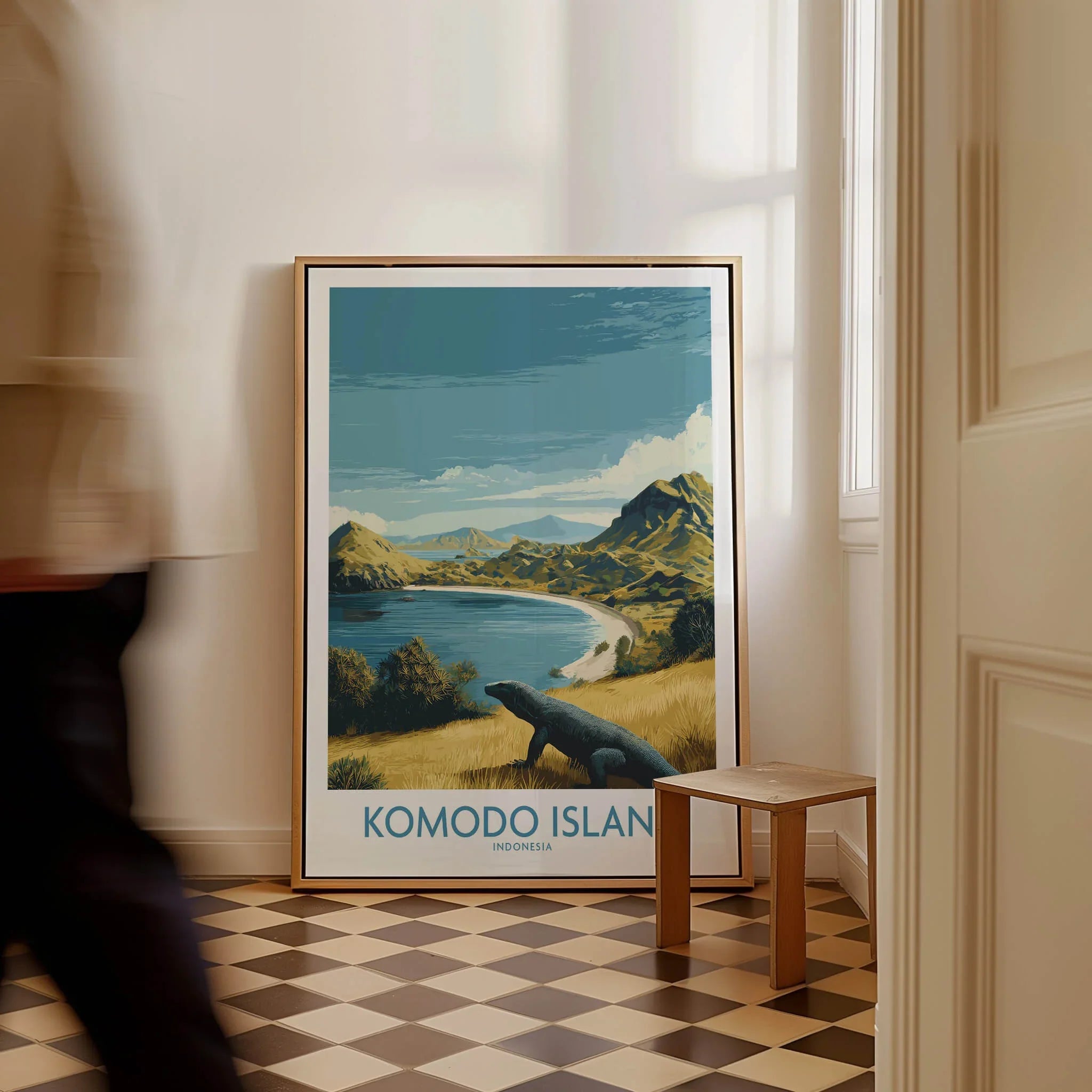 Framed Komodo Island travel poster with landscape art on floor, man walking past in hallway.