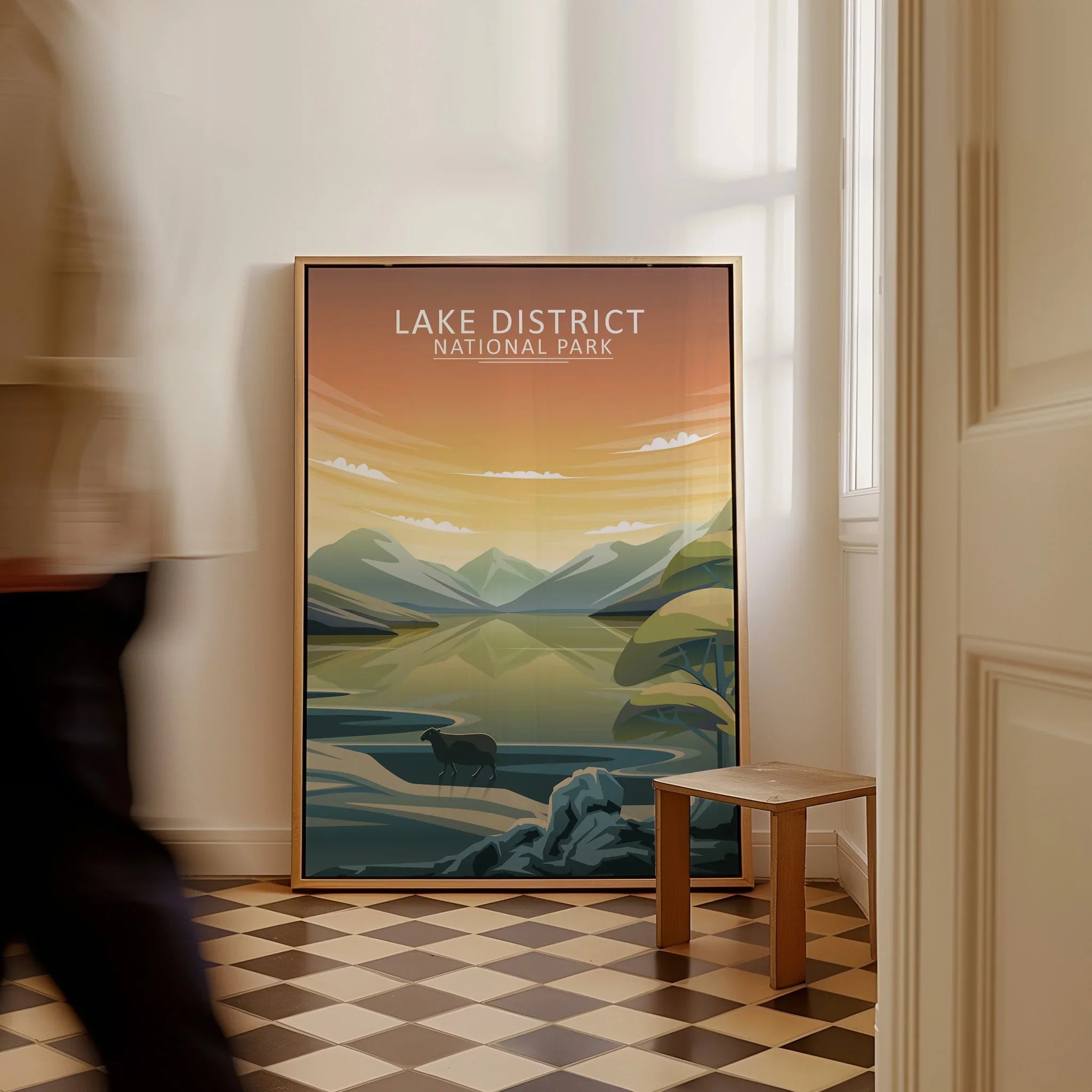 Framed Lake District National Park travel poster on floor in sunlit hallway, man walking by.