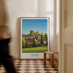 Framed Lewes England travel poster leaning on wall in bright hallway, man walking past