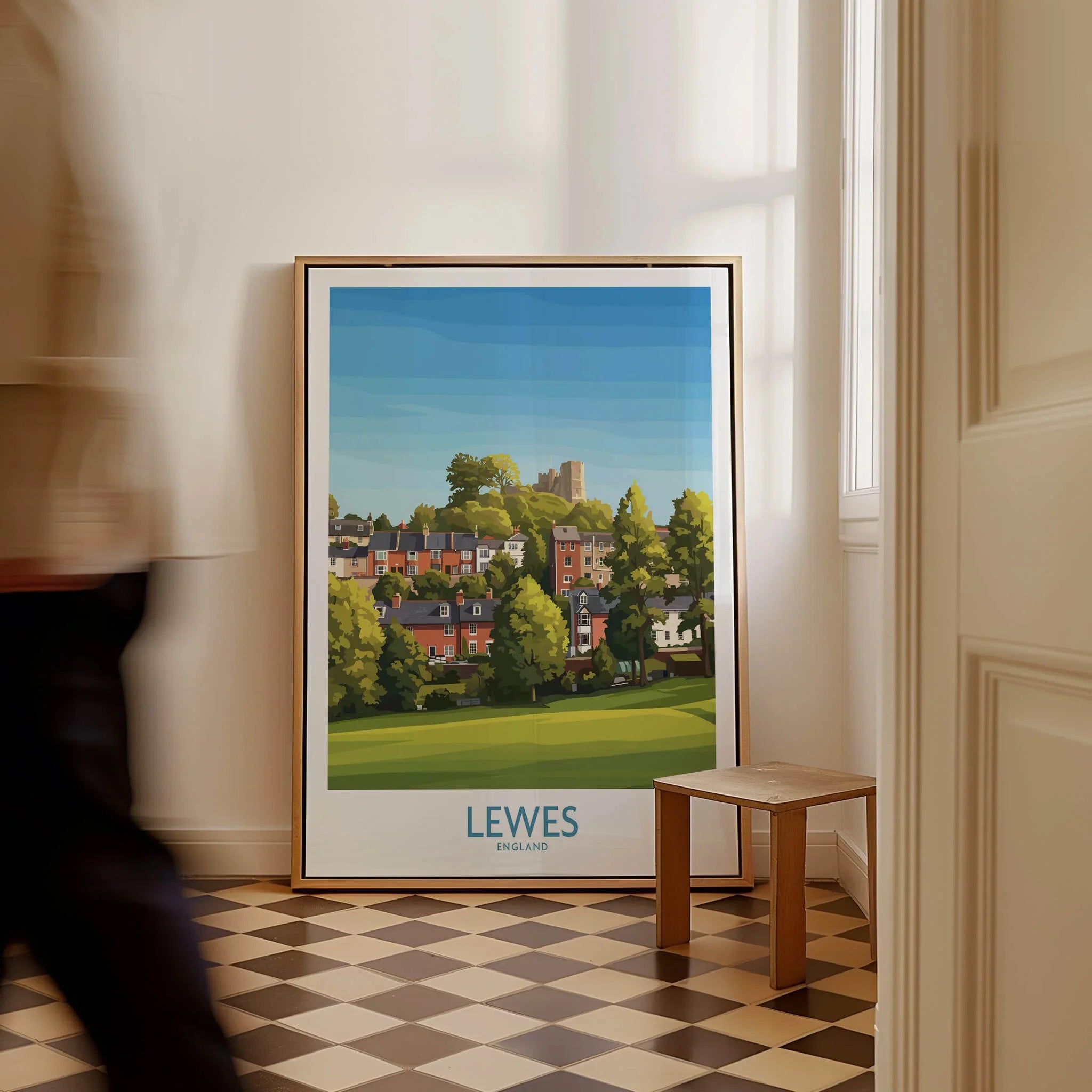 Framed Lewes England travel poster leaning on wall in bright hallway, man walking past