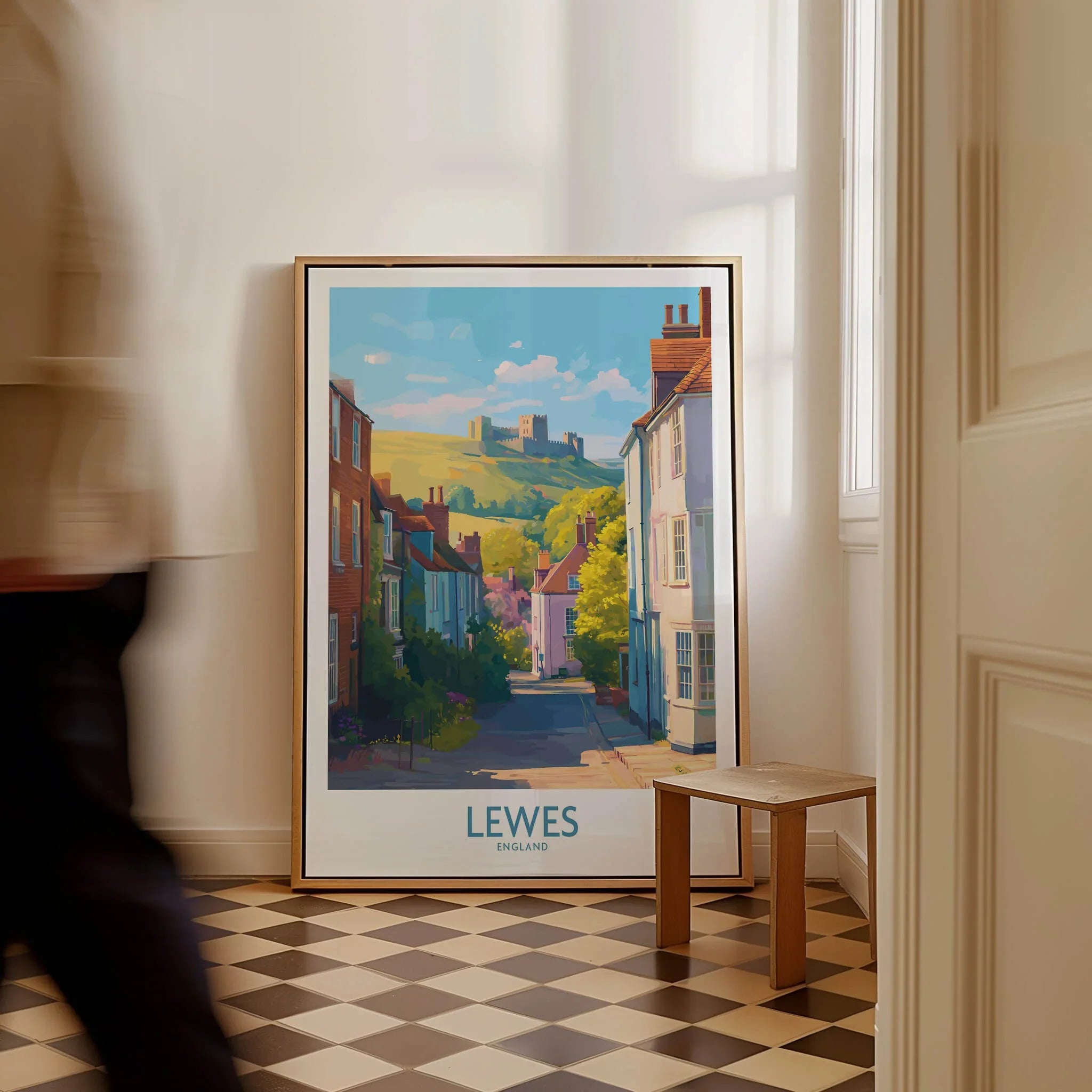 Framed Lewes England travel poster with town and castle, leaning on wall in bright room