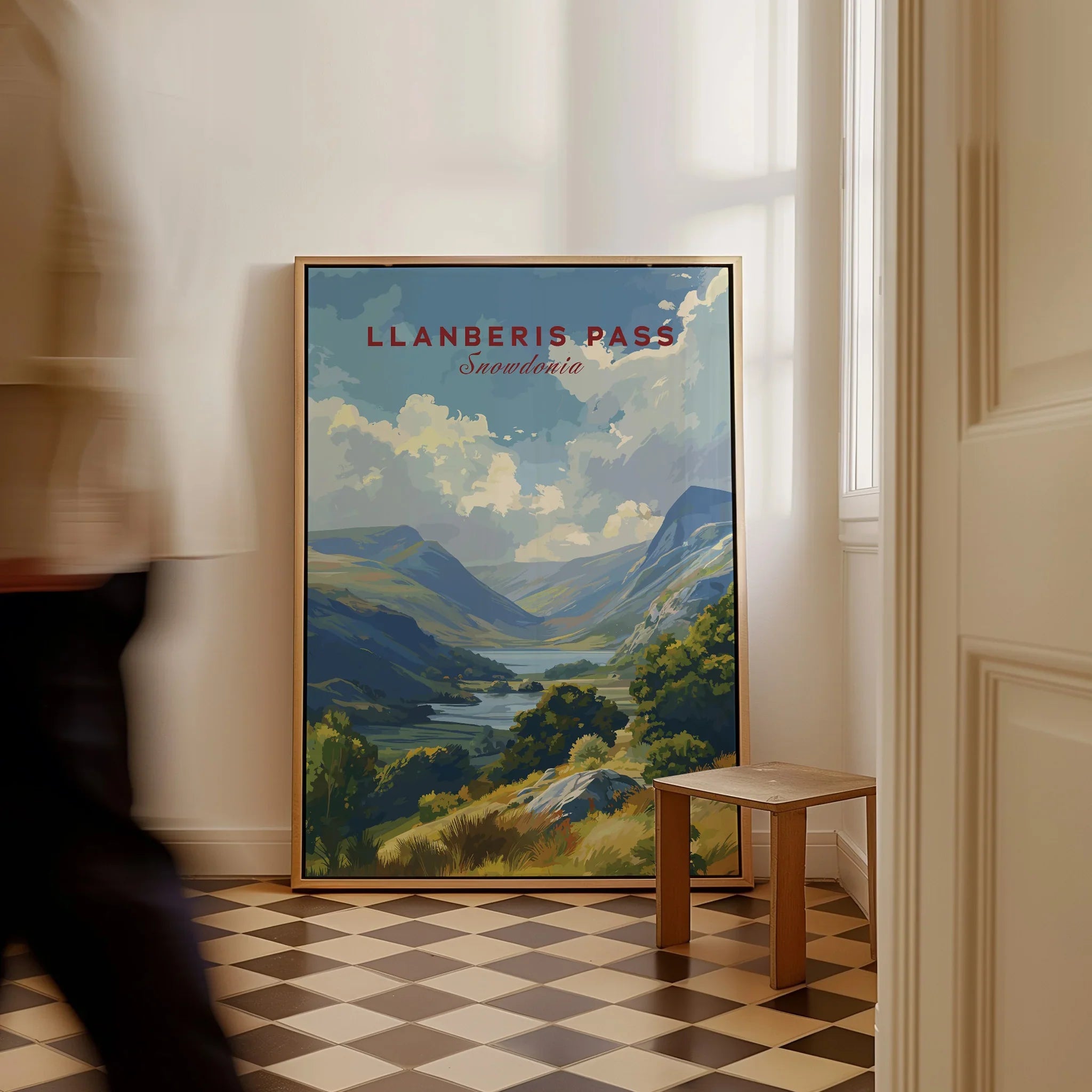 Framed Llanberis Pass Snowdonia travel poster on floor in bright hallway, man walking by